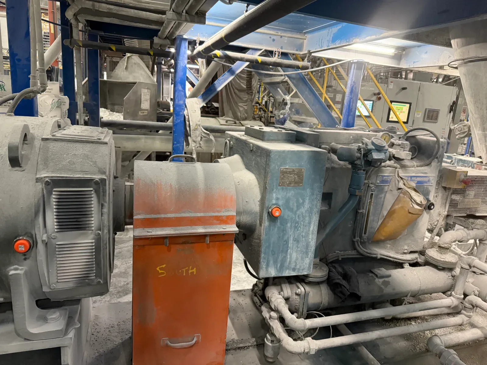 Gearbox and motor caked in lime dust inside a processing plant, with orange-capped PHANTOM® sensors still mounted and reporting